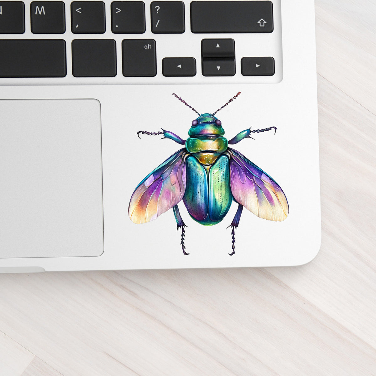 Flying Beetle With Open Wings UV DTF sticker applied to a silver laptop beside the keyboard