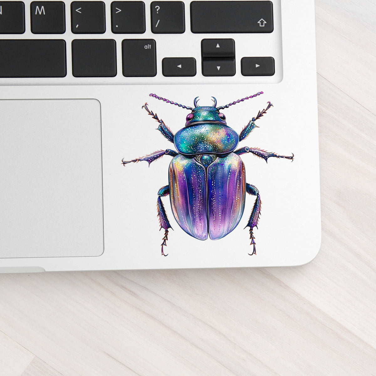 Violet Sparkle Beetle UV DTF sticker applied to a silver laptop beside the keyboard