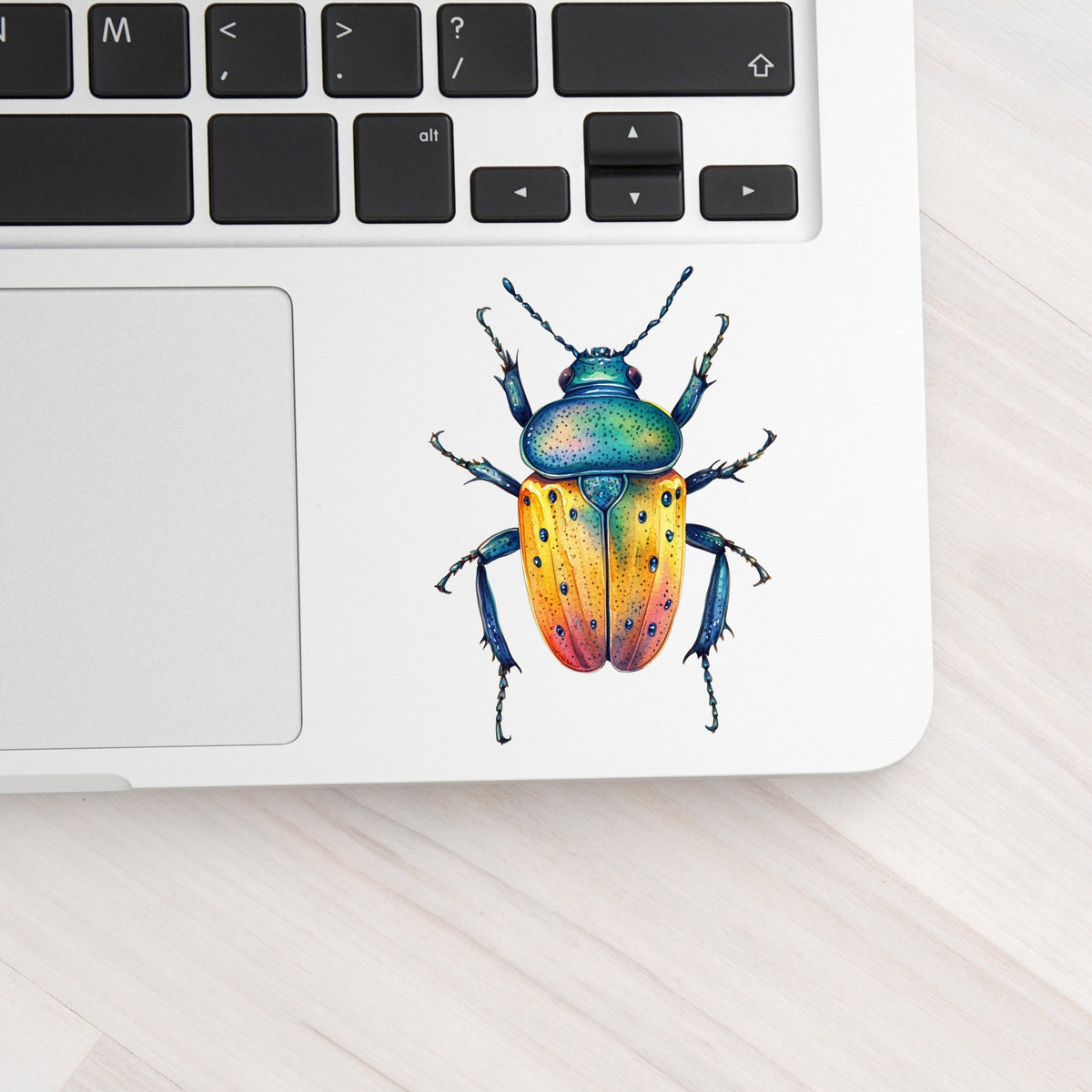 Orange And Blue Spotted Beetle UV DTF sticker applied to a silver laptop beside the keyboard