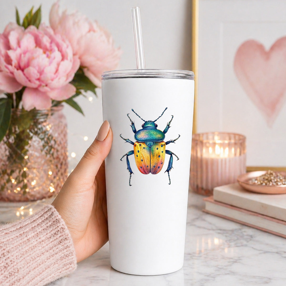 Orange And Blue Spotted Beetle UV DTF sticker applied to a white straw tumbler beside pink peonies