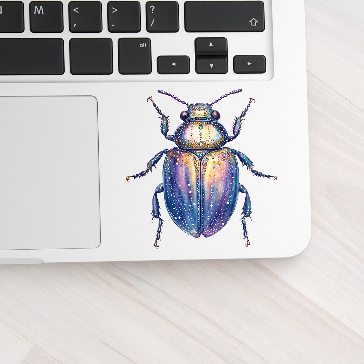 Lavender Jeweled Beetle UV DTF sticker applied to a silver laptop beside the keyboard
