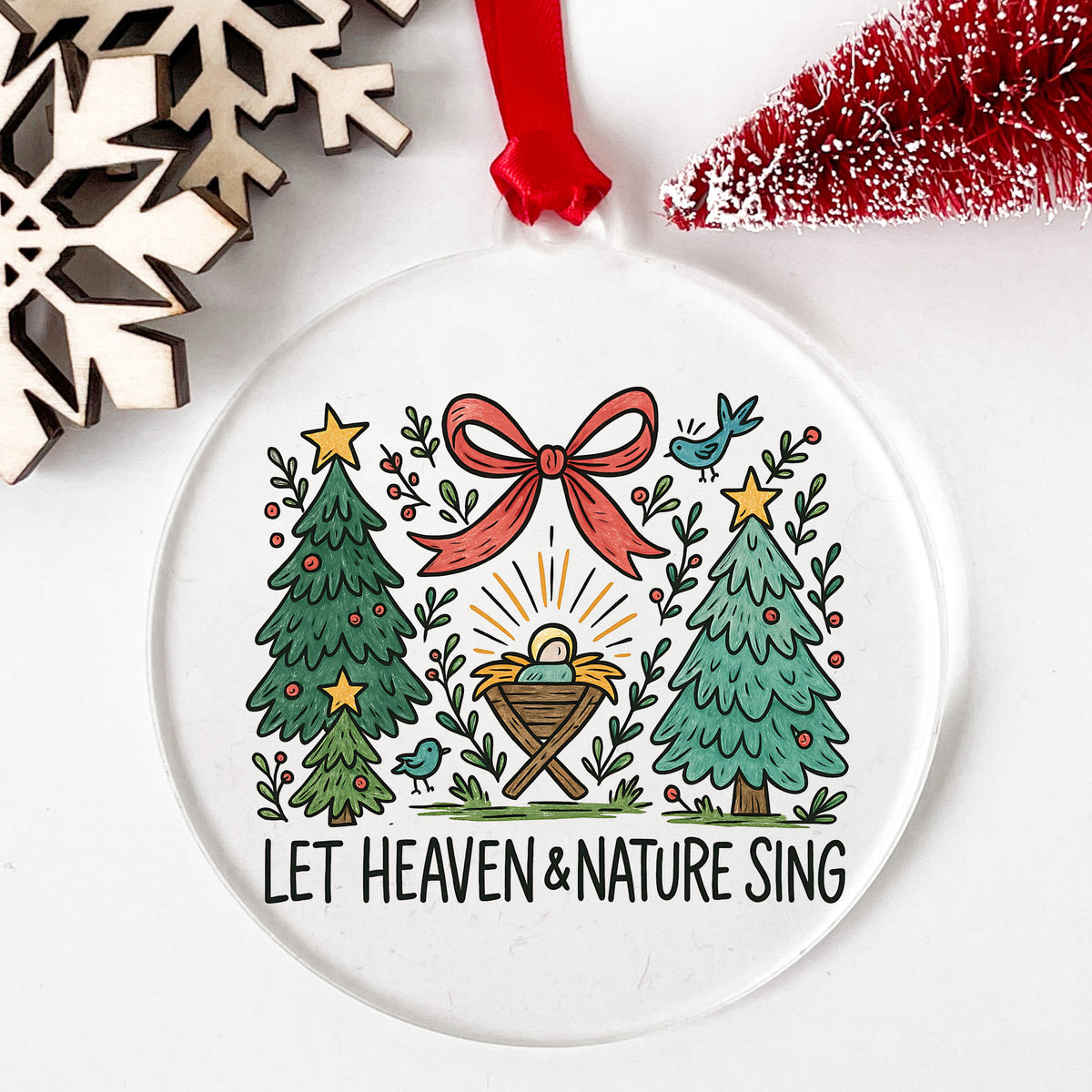 Let Heaven And Nature Sing Nativity UV DTF sticker applied to a clear round acrylic ornament with a red ribbon