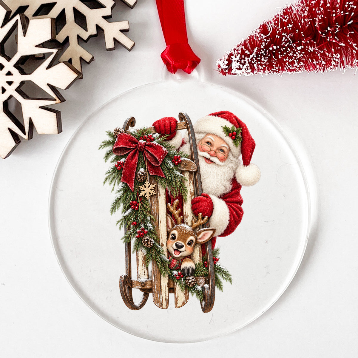 Santa And Reindeer With Wooden Sled UV DTF sticker applied to a clear round acrylic ornament with a red ribbon