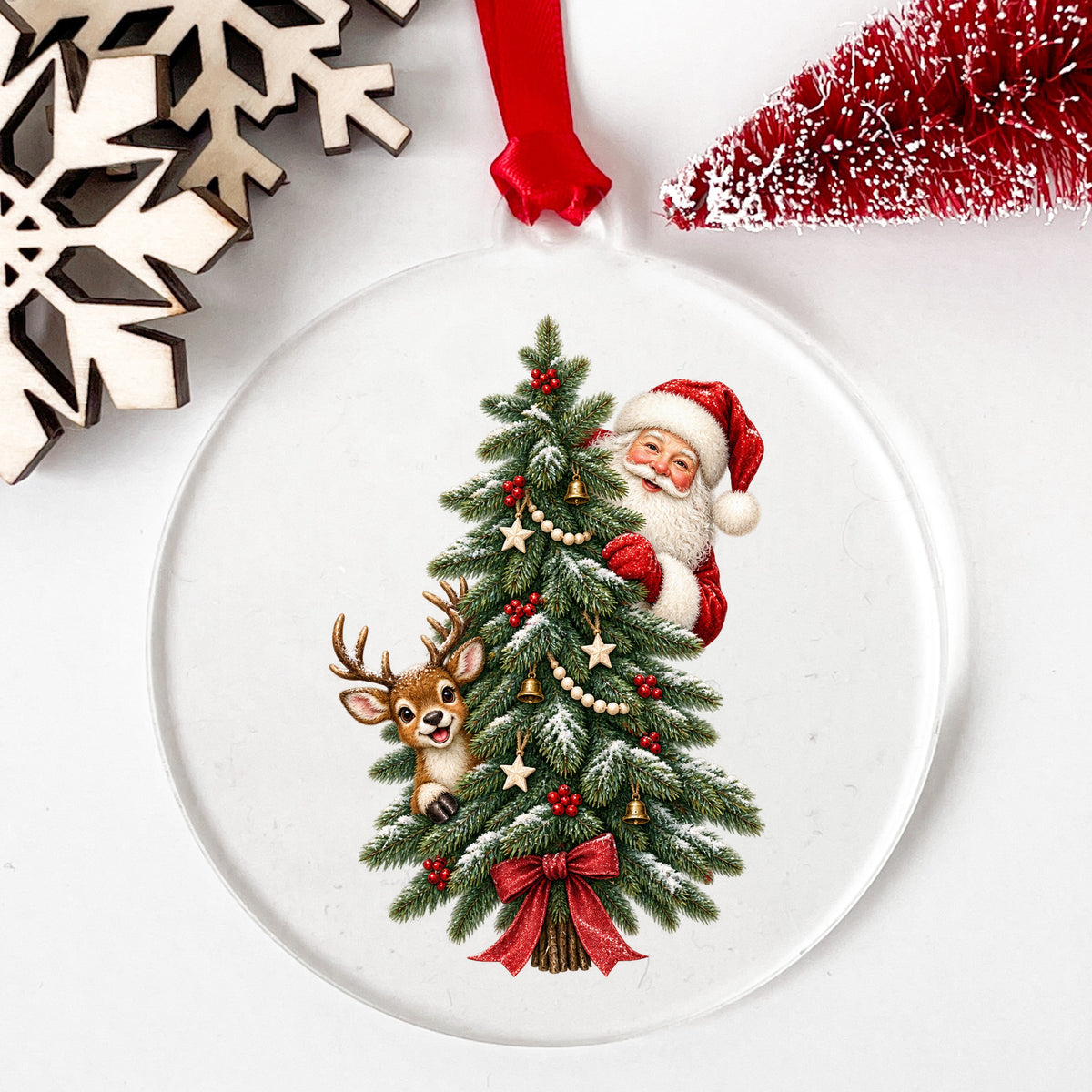 Santa And Reindeer Peeking Behind Christmas Tree UV DTF sticker applied to a clear round acrylic ornament with a red ribbon