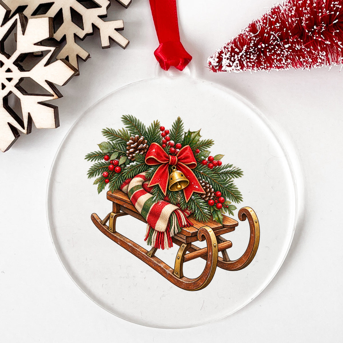 Vintage Wooden Sled With Greenery UV DTF sticker applied to a clear round acrylic ornament with a red ribbon