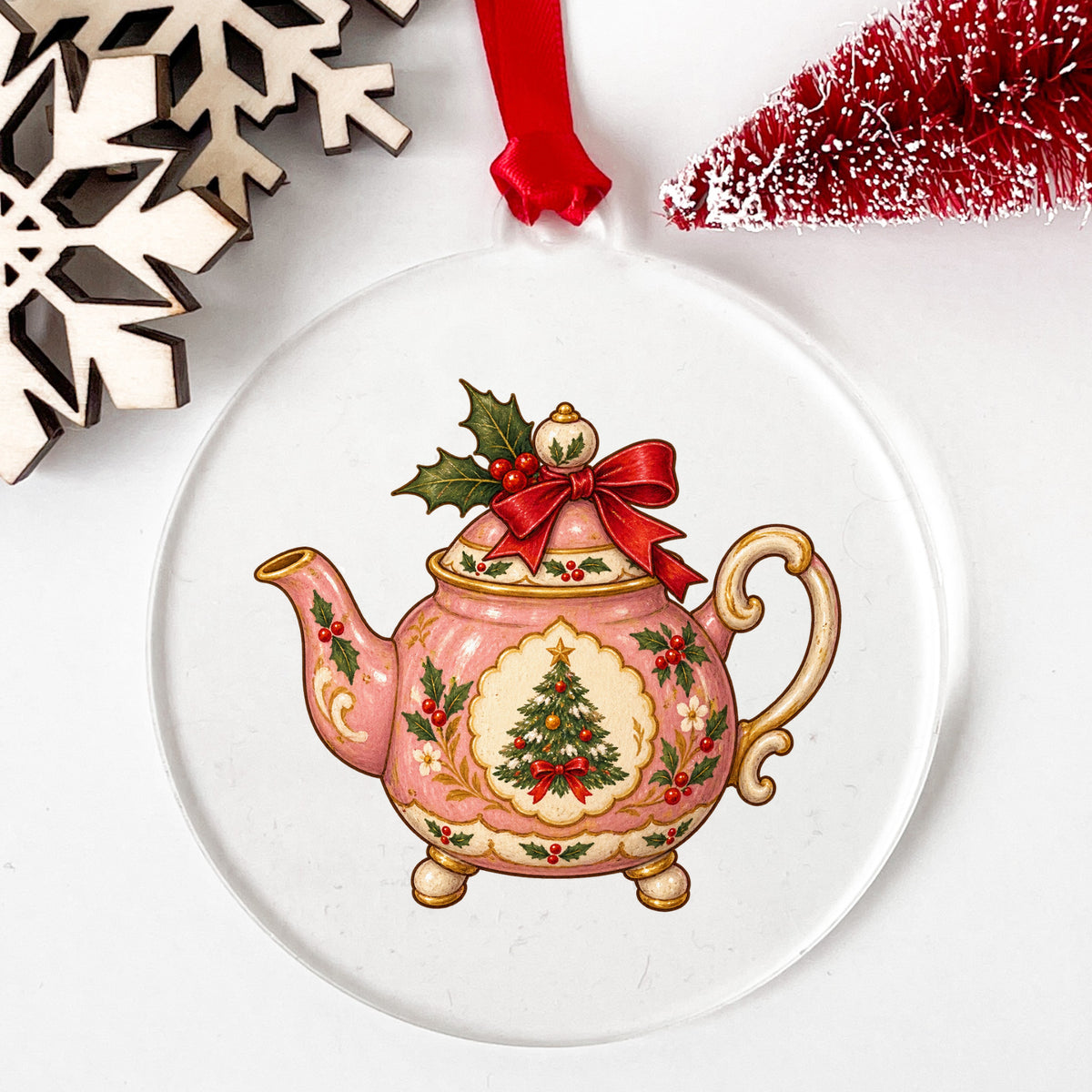 Pink Christmas Teapot With Holly UV DTF sticker applied to a clear round acrylic ornament with a red ribbon
