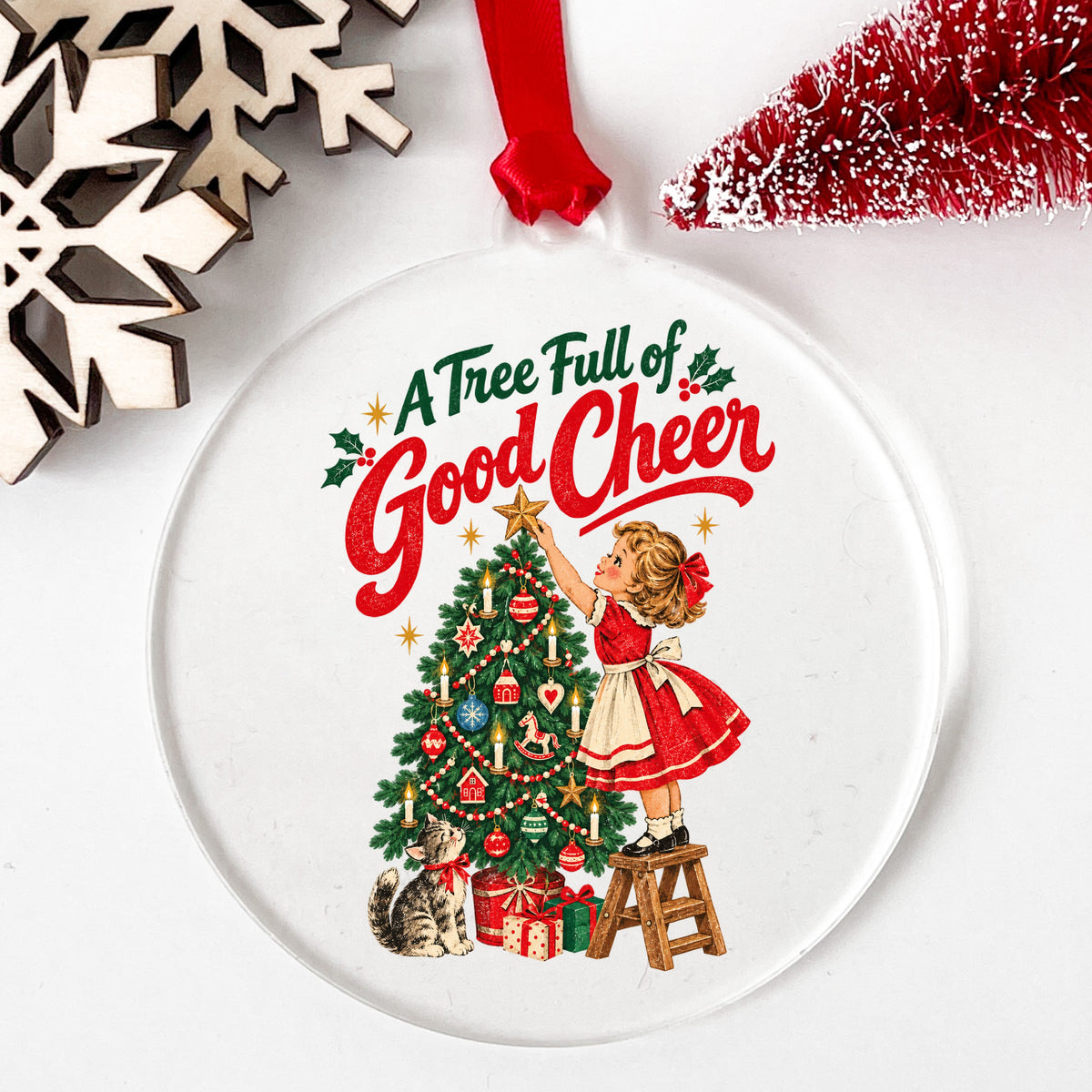 A Tree Full Of Good Cheer UV DTF sticker applied to a clear round acrylic ornament with a red ribbon