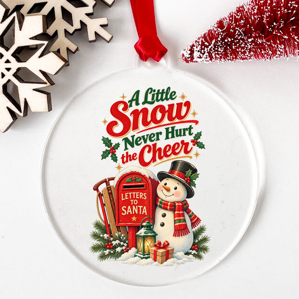 A Little Snow Never Hurt The Cheer Snowman UV DTF sticker applied to a clear round acrylic ornament with a red ribbon