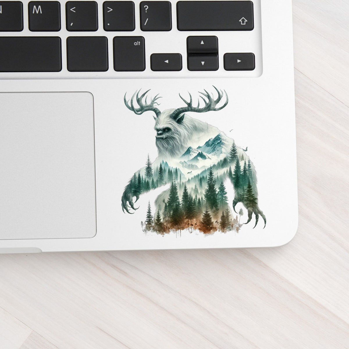 Antlered Mountain Bigfoot UV DTF sticker applied to a silver laptop beside the keyboard