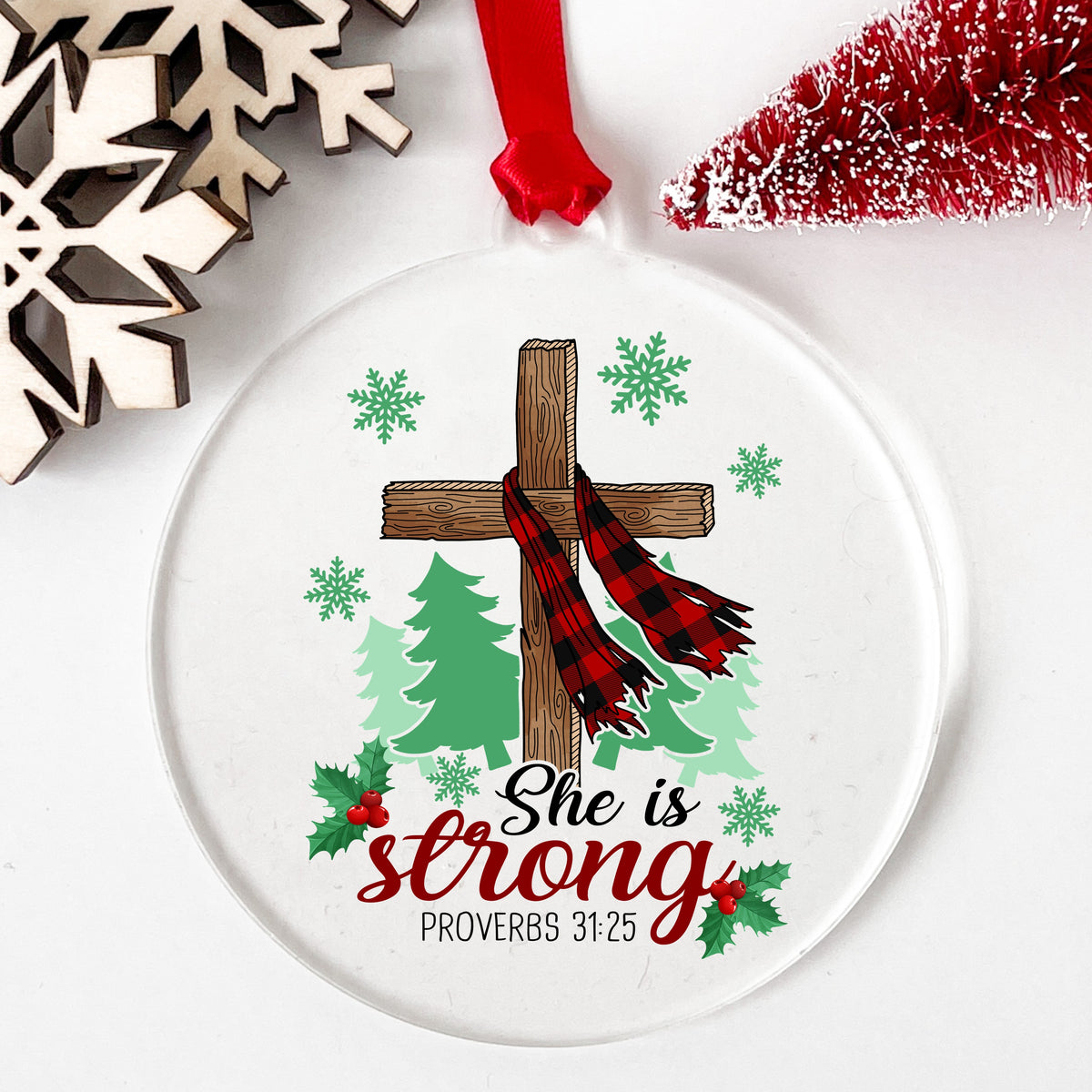 She Is Strong Christmas Cross UV DTF sticker applied to a clear round acrylic ornament with a red ribbon