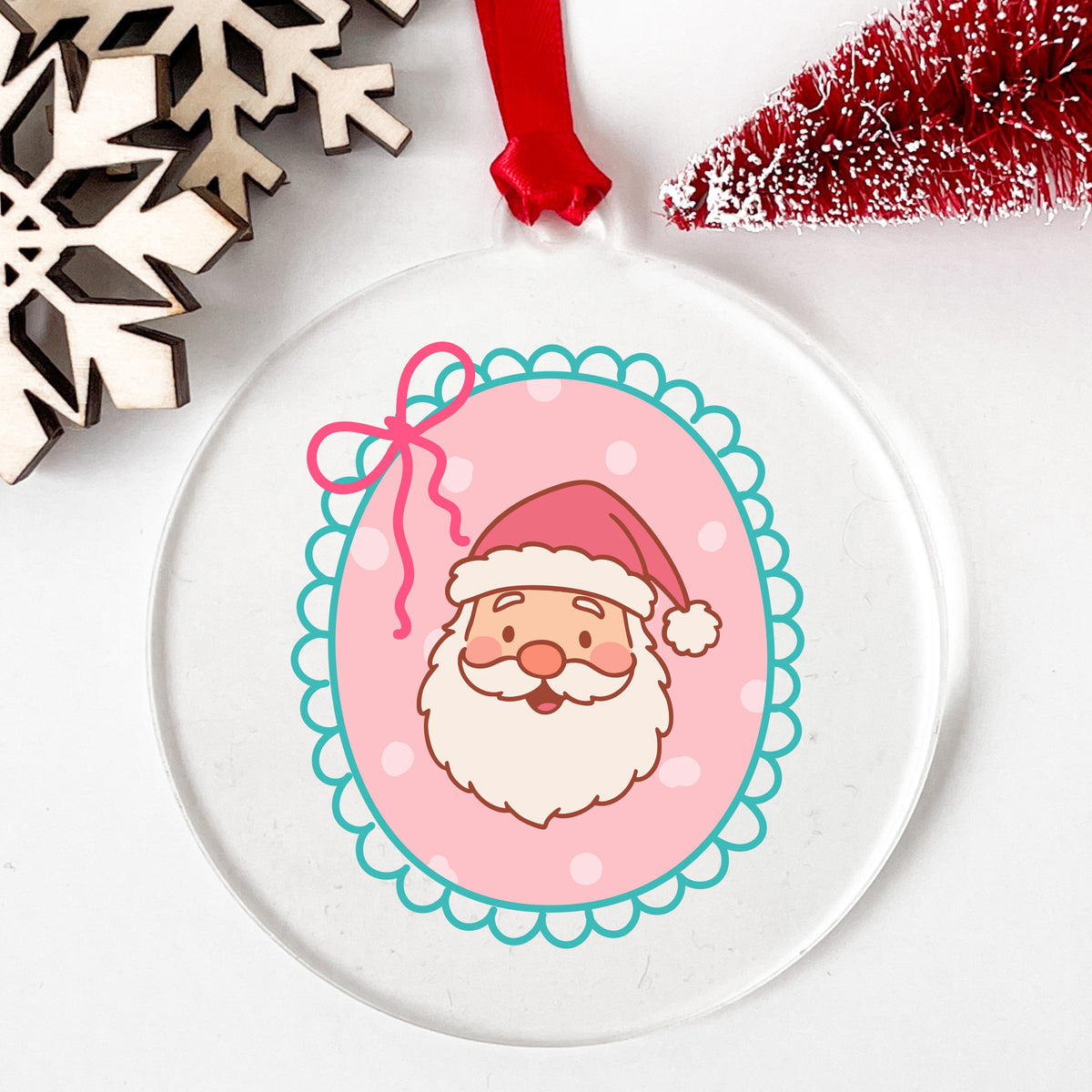 Coquette Pink Santa Claus Face UV DTF sticker applied to a clear round acrylic ornament with a red ribbon