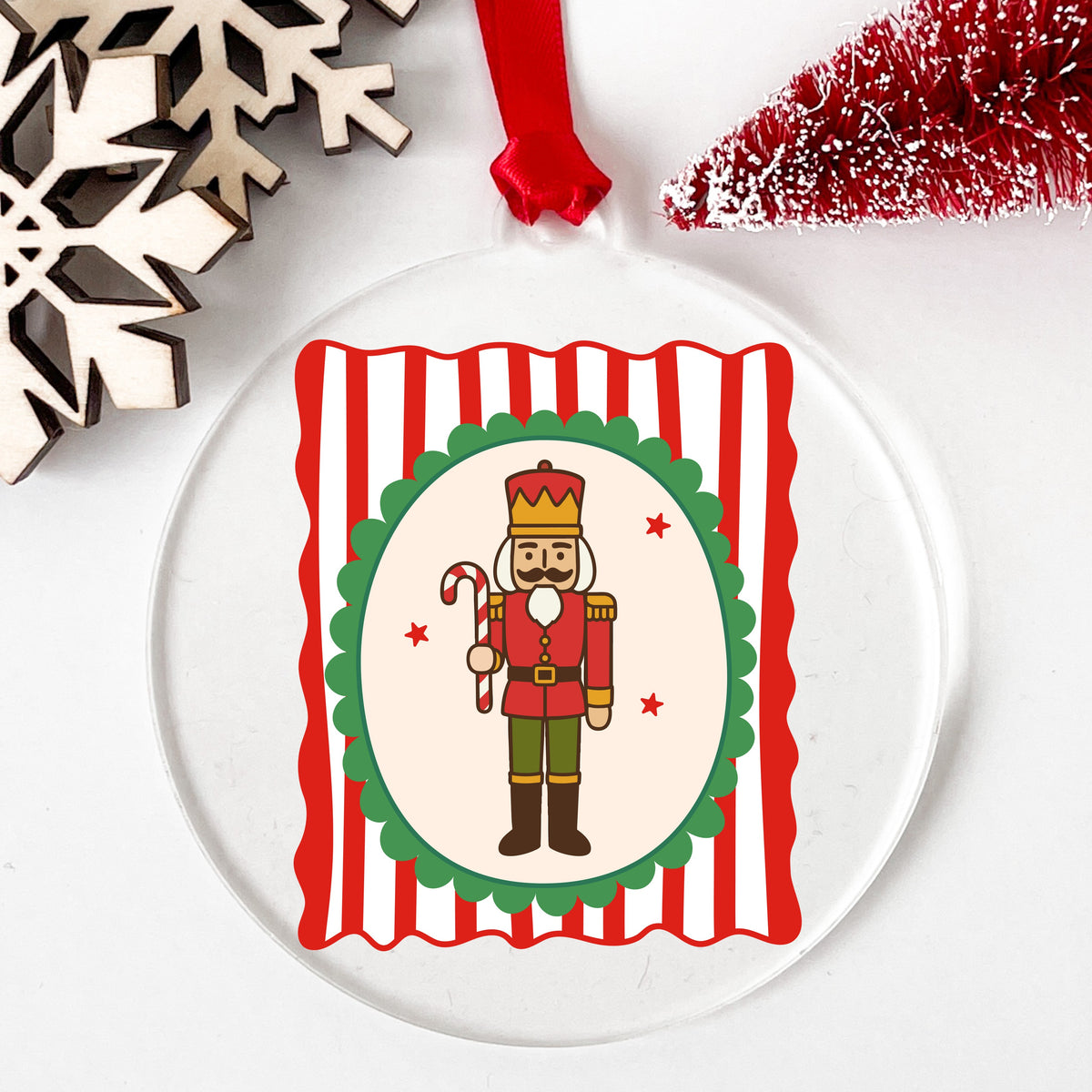 Coquette Nutcracker Soldier UV DTF sticker applied to a clear round acrylic ornament with a red ribbon