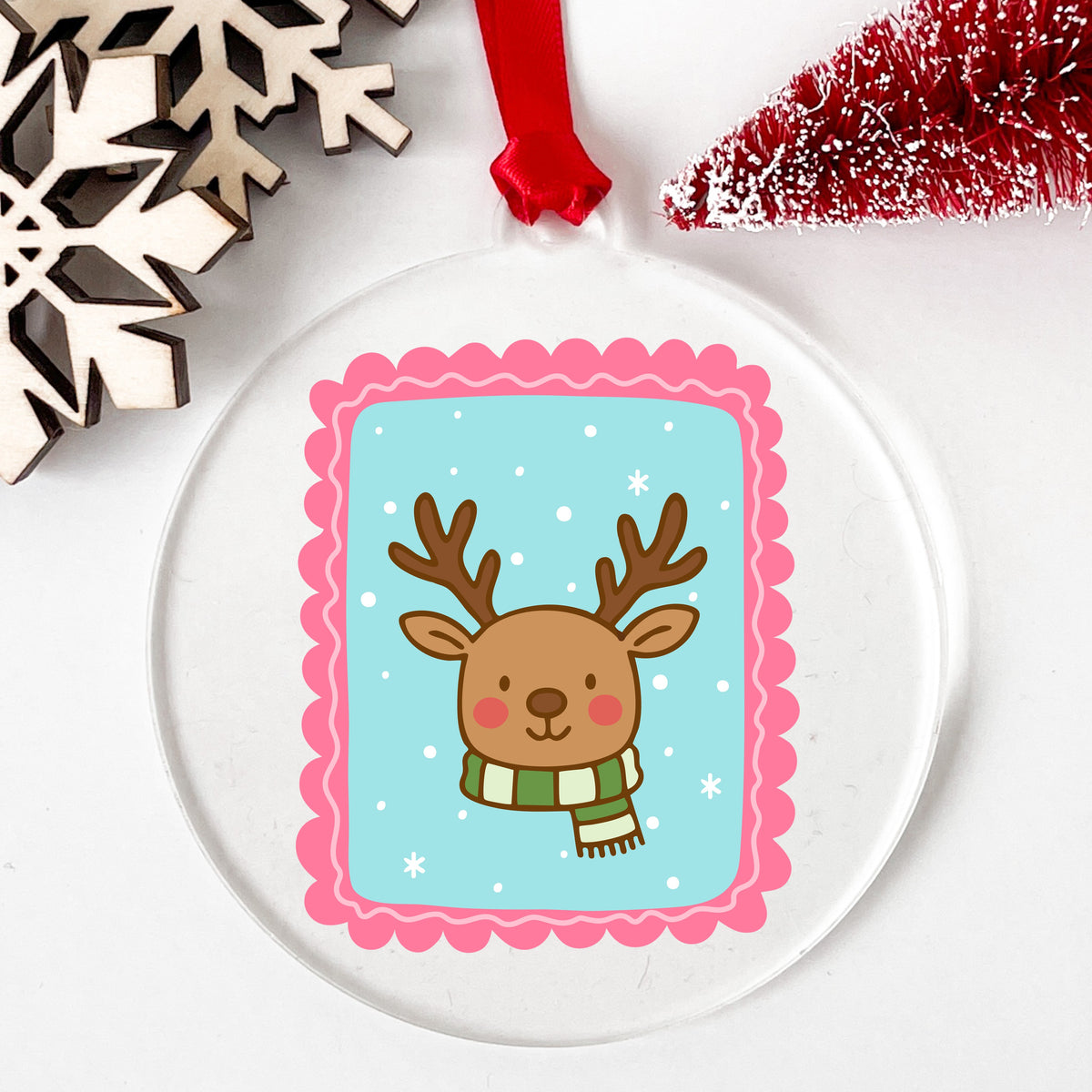 Coquette Reindeer Face UV DTF sticker applied to a clear round acrylic ornament with a red ribbon