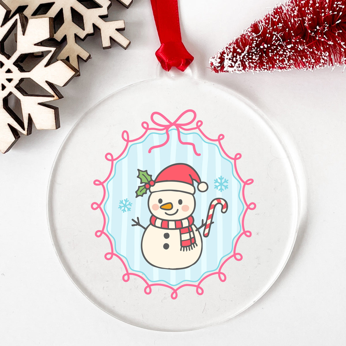 Coquette Snowman Candy Cane UV DTF sticker applied to a clear round acrylic ornament with a red ribbon