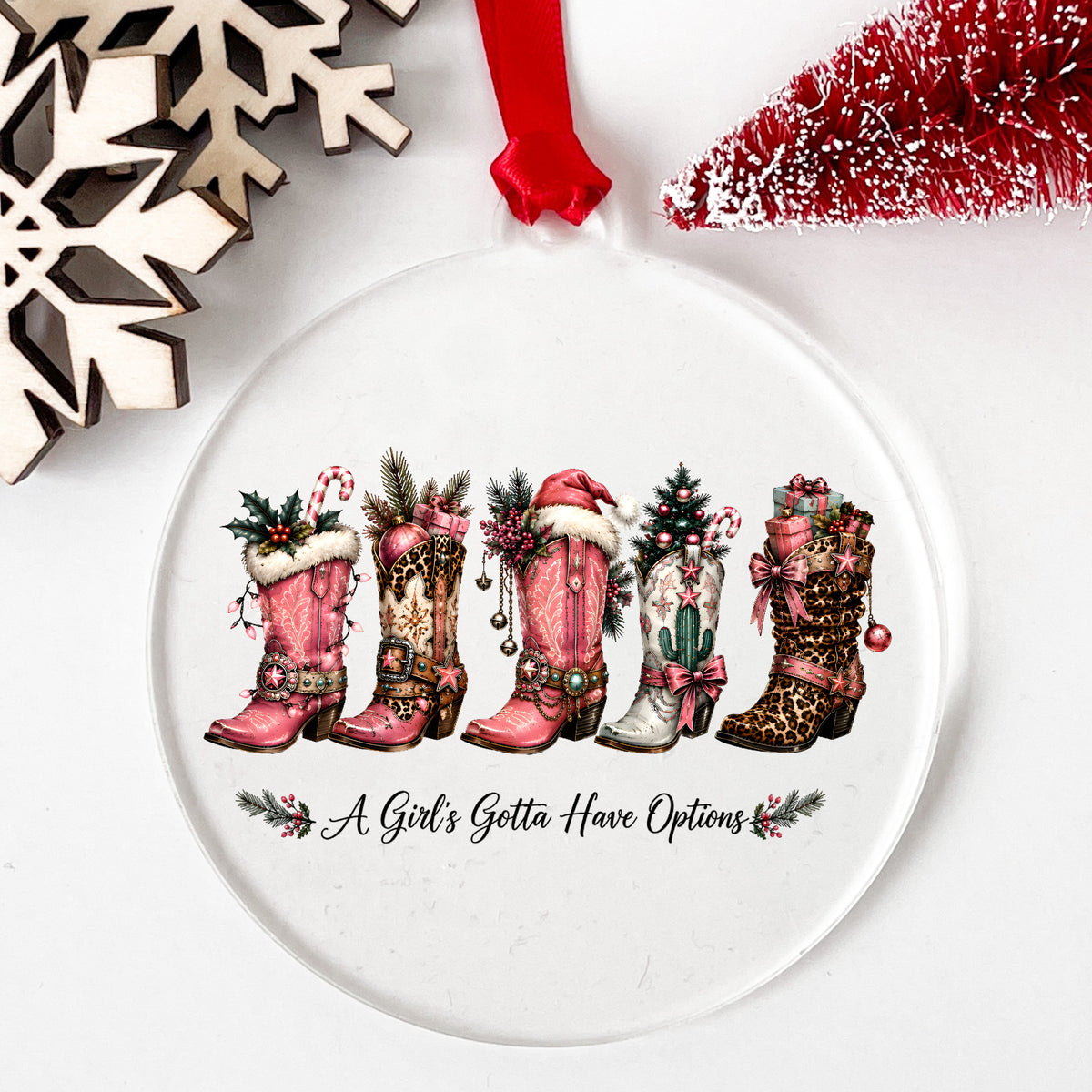 A Girls Gotta Have Options Christmas Boots UV DTF sticker applied to a clear round acrylic ornament with a red ribbon