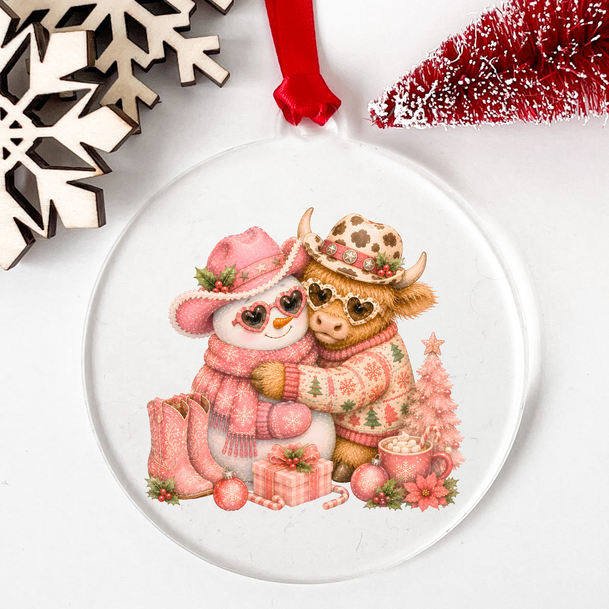 Snowman Highland Cow Christmas Hug UV DTF sticker applied to a clear round acrylic ornament with a red ribbon