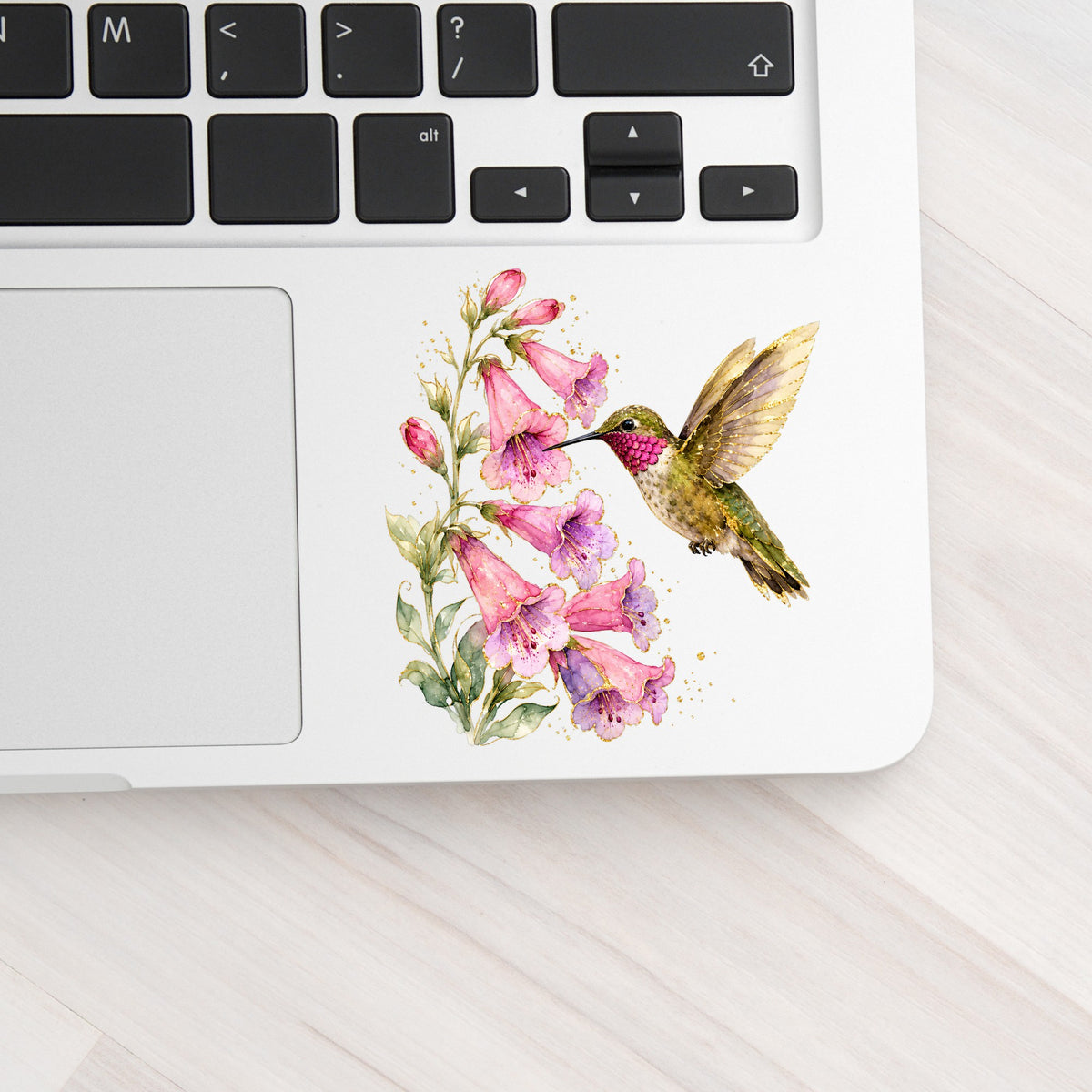 Ruby Throated Hummingbird Pink Bells UV DTF sticker applied to a silver laptop beside the keyboard
