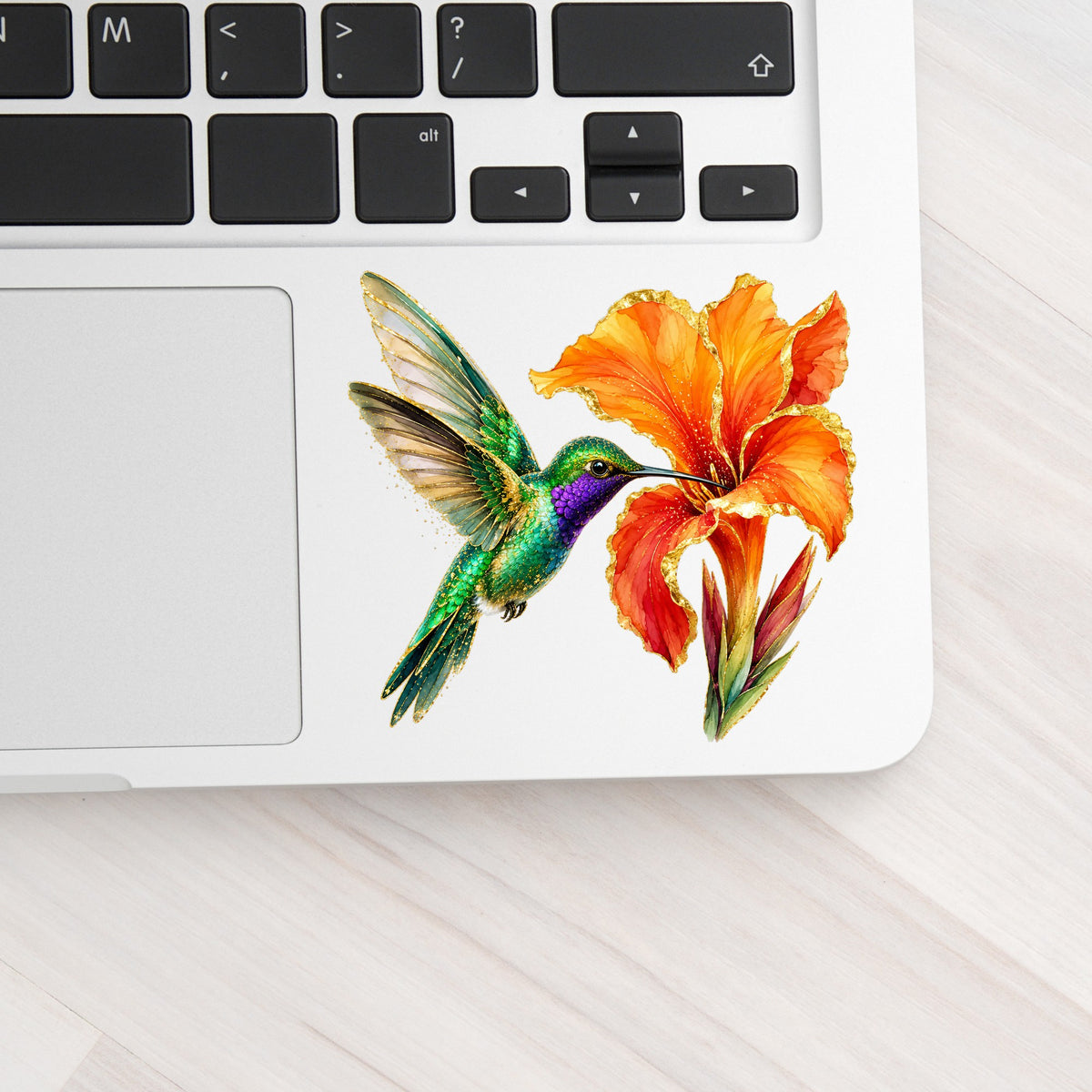 Hummingbird Orange Canna Lily UV DTF sticker applied to a silver laptop beside the keyboard