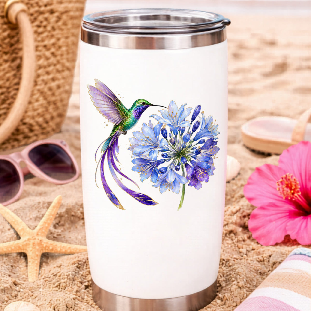 Hummingbird Blue Agapanthus UV DTF sticker applied to a white travel tumbler on beach sand