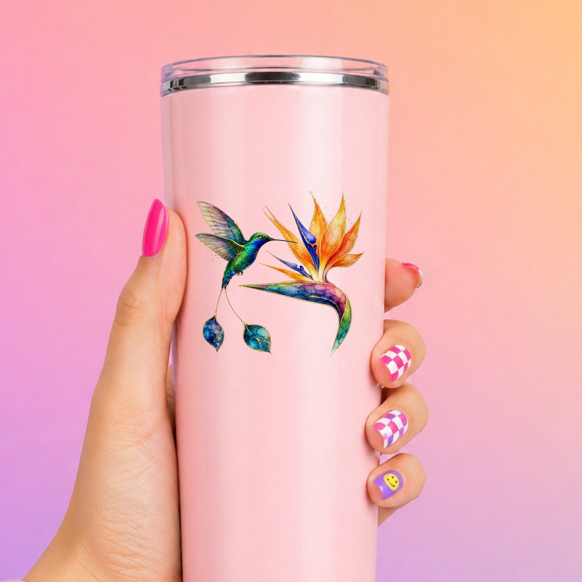 Hummingbird Bird Of Paradise Flower UV DTF sticker applied to a tall pink tumbler on a pink and orange background