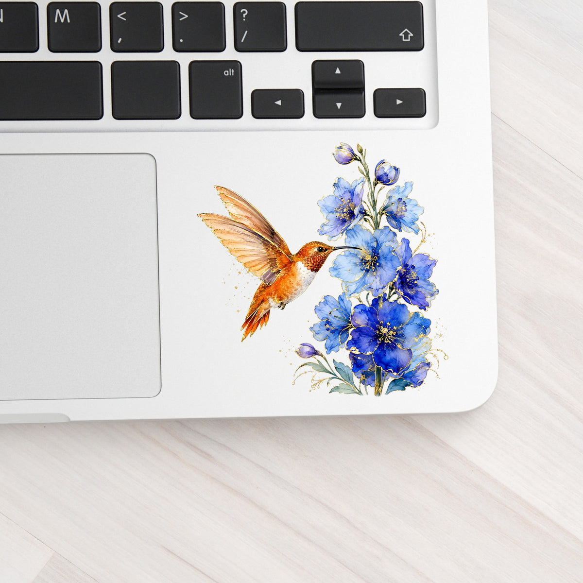 Rufous Hummingbird Blue Delphinium UV DTF sticker applied to a silver laptop beside the keyboard