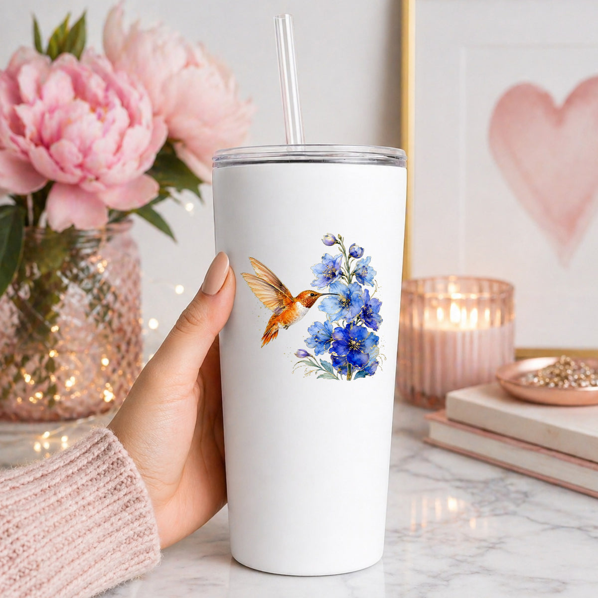 Rufous Hummingbird Blue Delphinium UV DTF sticker applied to a white straw tumbler beside pink peonies
