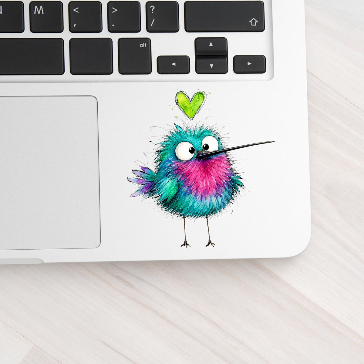 Fluffy Teal Pink Hummingbird UV DTF sticker applied to a silver laptop beside the keyboard