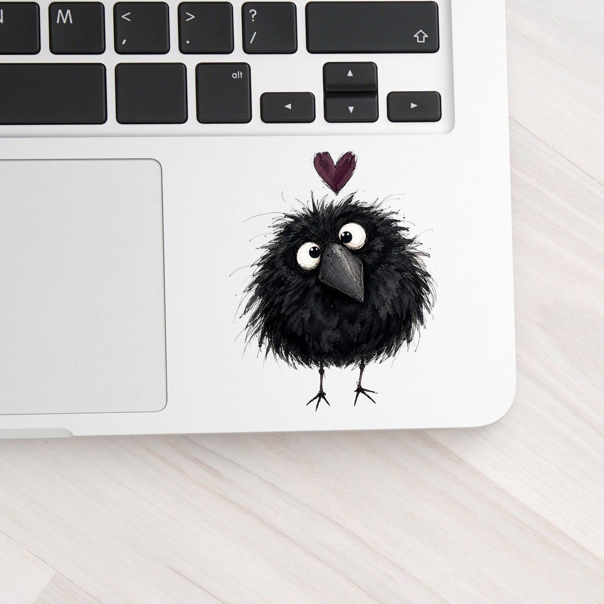 Fluffy Black Crow UV DTF sticker applied to a silver laptop beside the keyboard