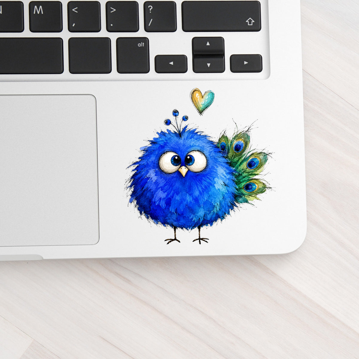 Blue Peacock Crest UV DTF sticker applied to a silver laptop beside the keyboard