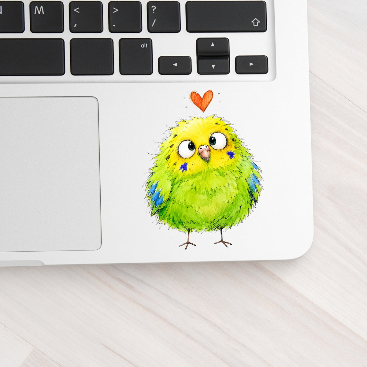 Funny Green Budgie UV DTF sticker applied to a silver laptop beside the keyboard