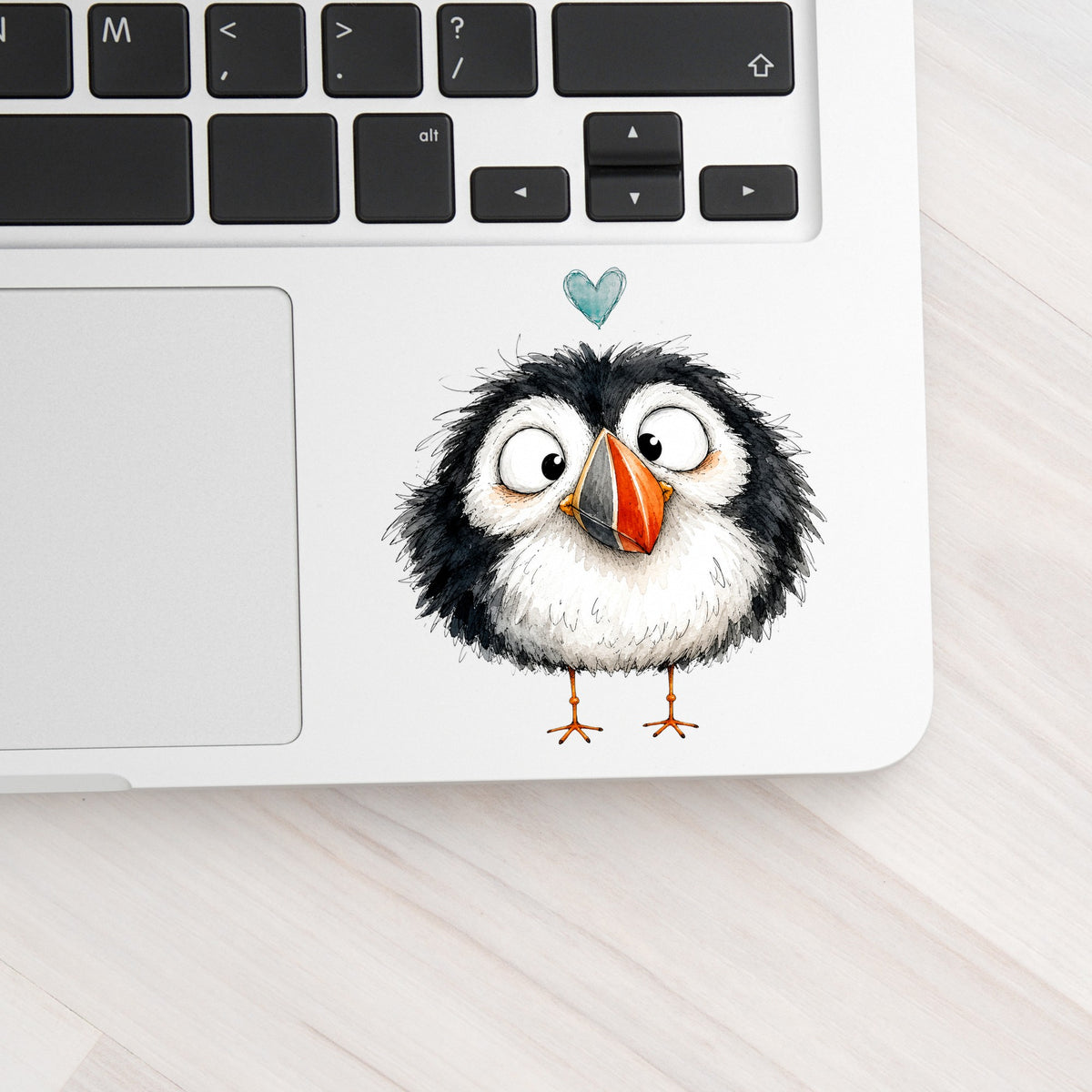 Cartoon Puffin UV DTF sticker applied to a silver laptop beside the keyboard