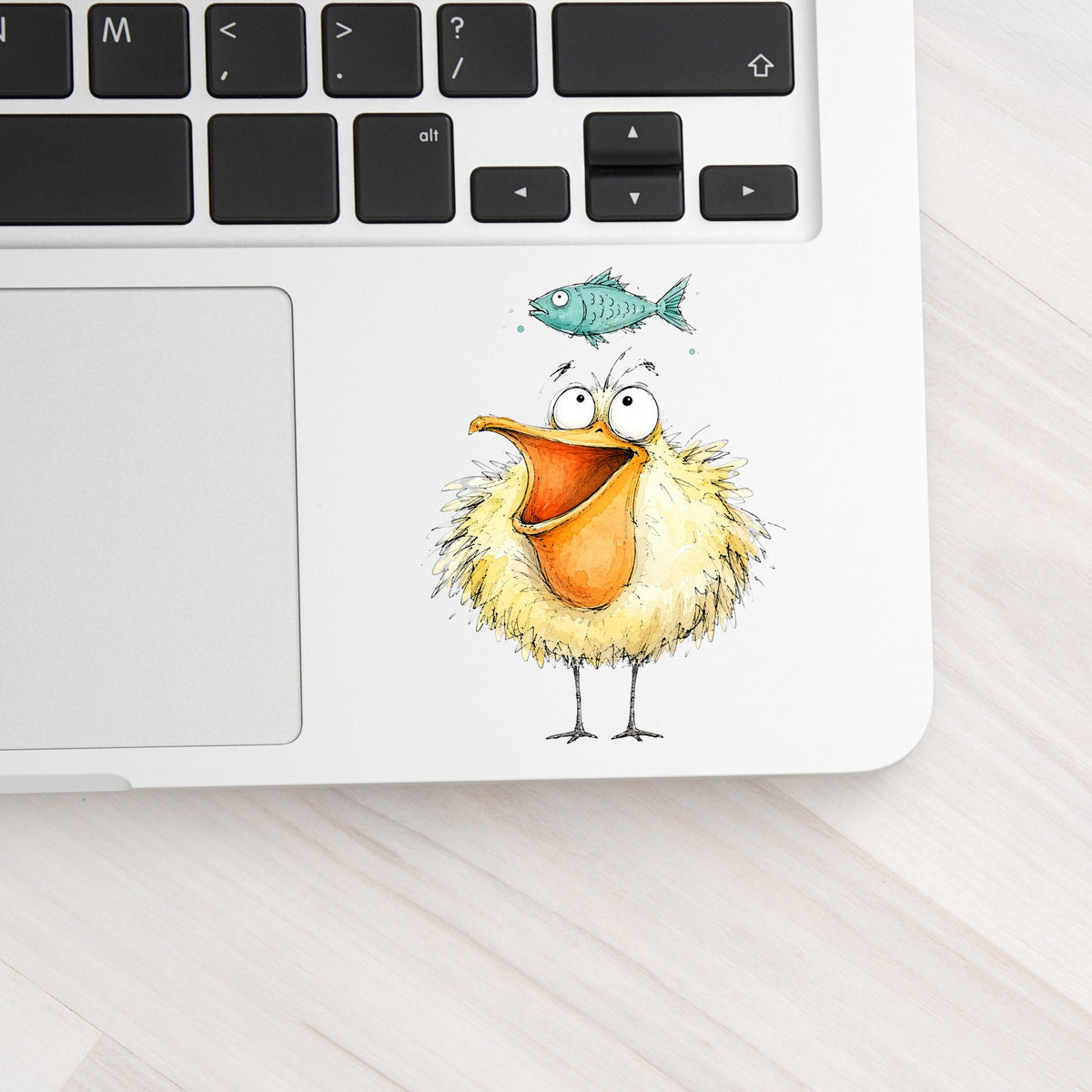 Funny Pelican With Fish UV DTF sticker applied to a silver laptop beside the keyboard