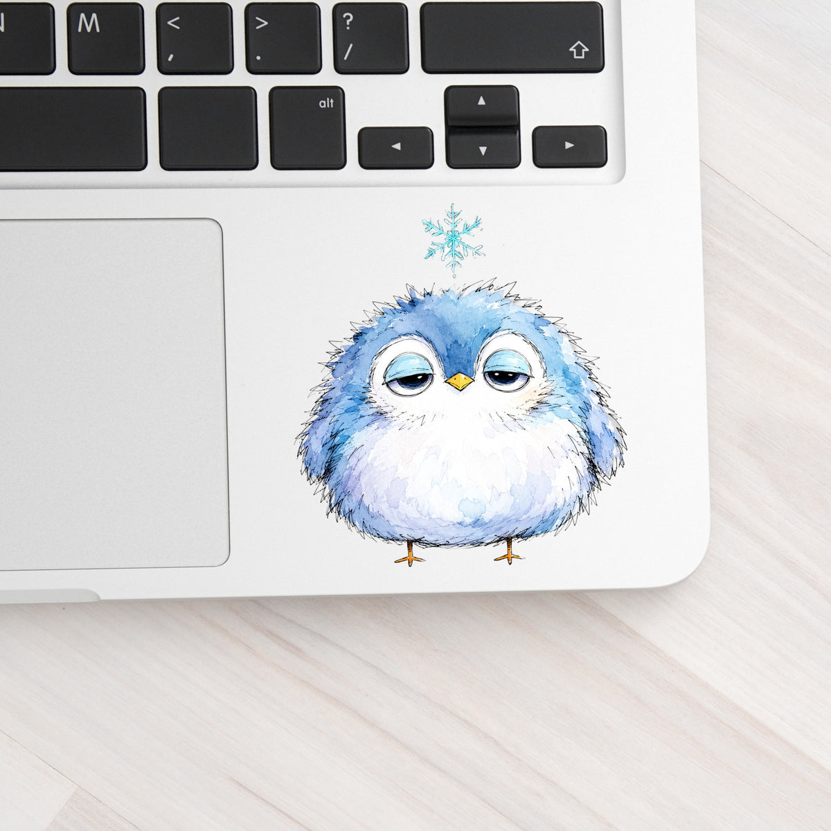 Sleepy Blue Bird Snowflake UV DTF sticker applied to a silver laptop beside the keyboard