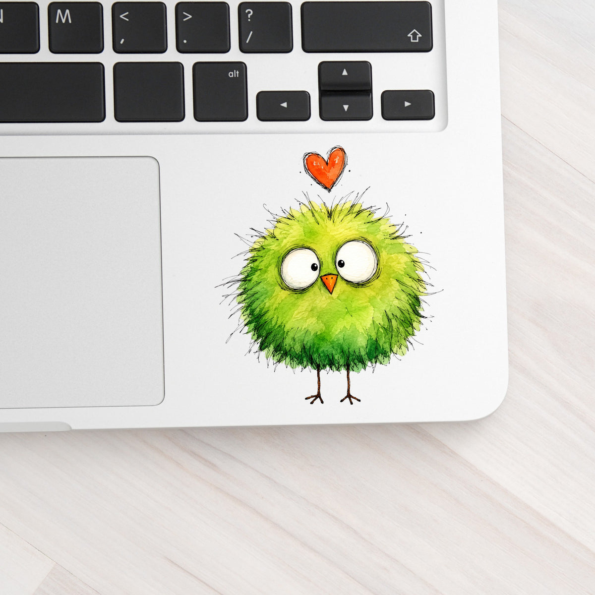 Fluffy Green Bird UV DTF sticker applied to a silver laptop beside the keyboard