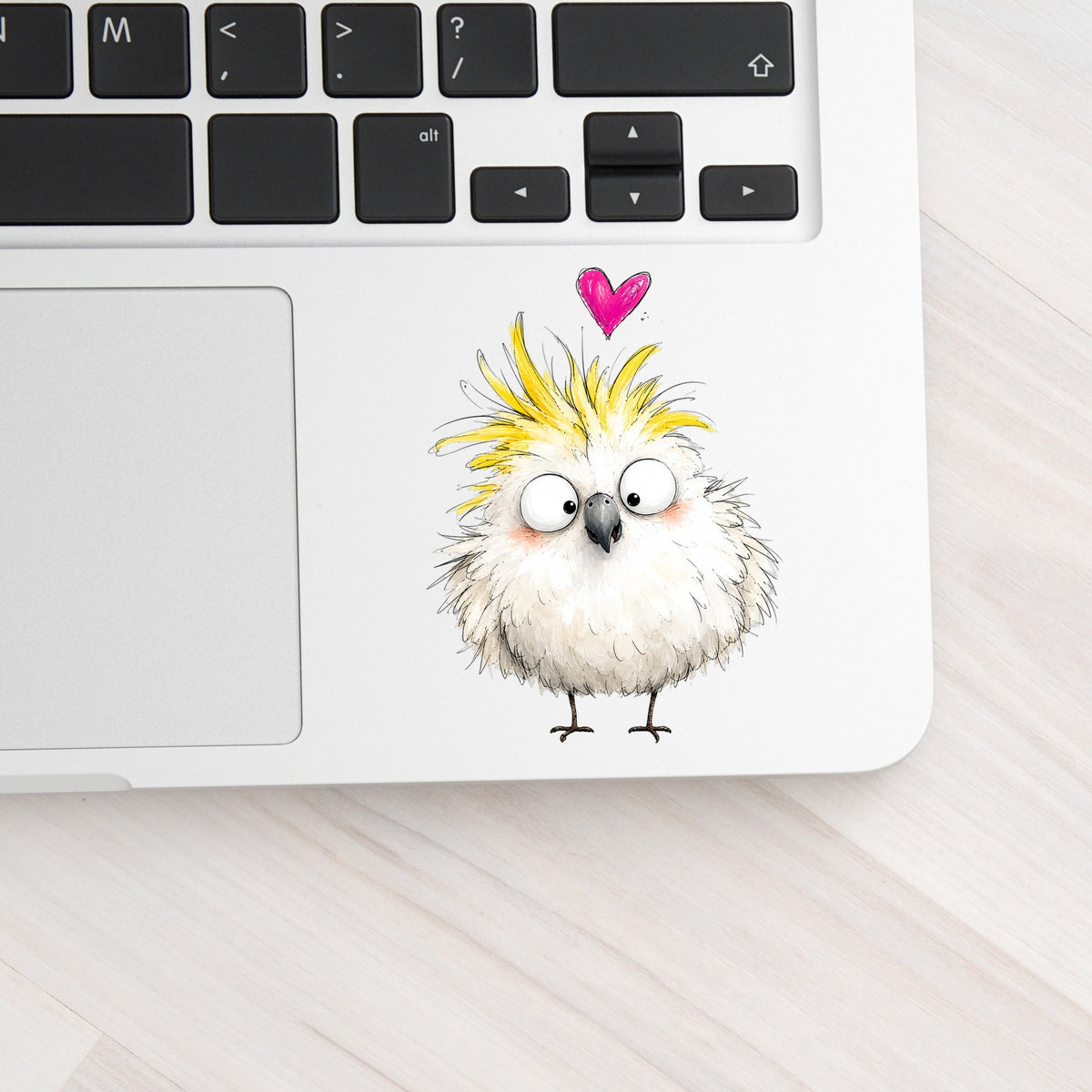 Cartoon Cockatoo Parrot UV DTF sticker applied to a silver laptop beside the keyboard