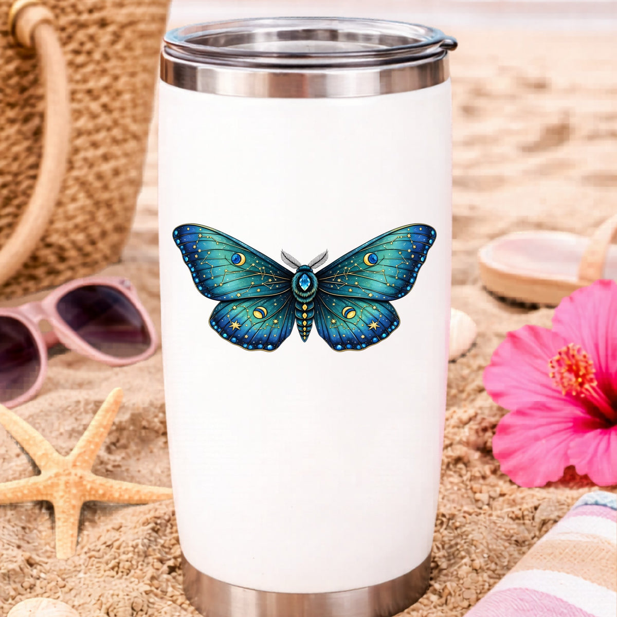 Teal Celestial Moth UV DTF sticker applied to a white travel tumbler on beach sand