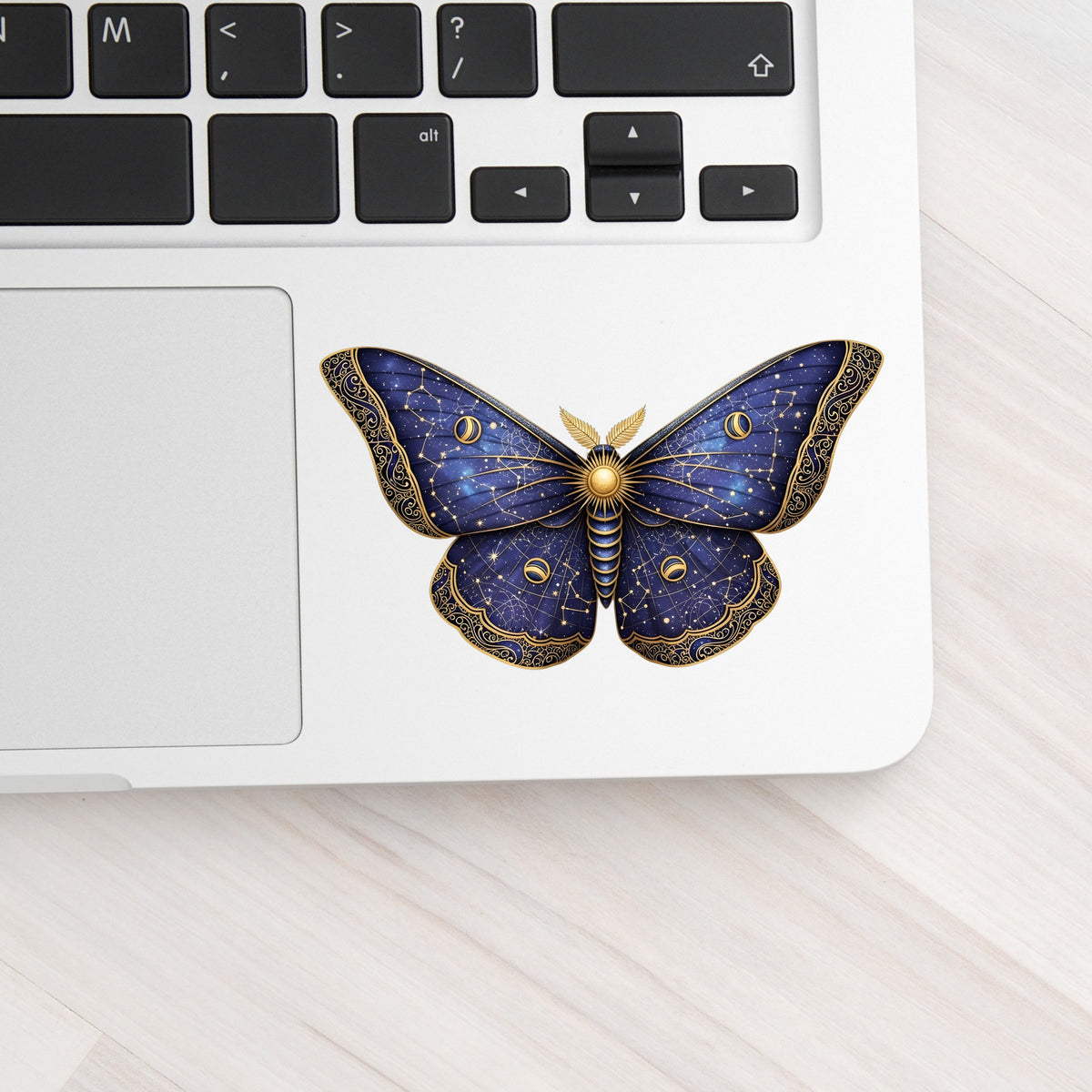 Navy Constellation Moth UV DTF sticker applied to a silver laptop beside the keyboard