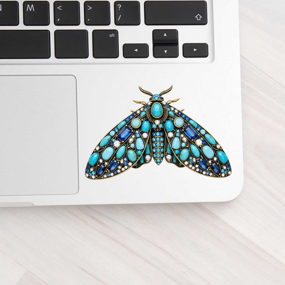 Turquoise Jeweled Moth UV DTF sticker applied to a silver laptop beside the keyboard