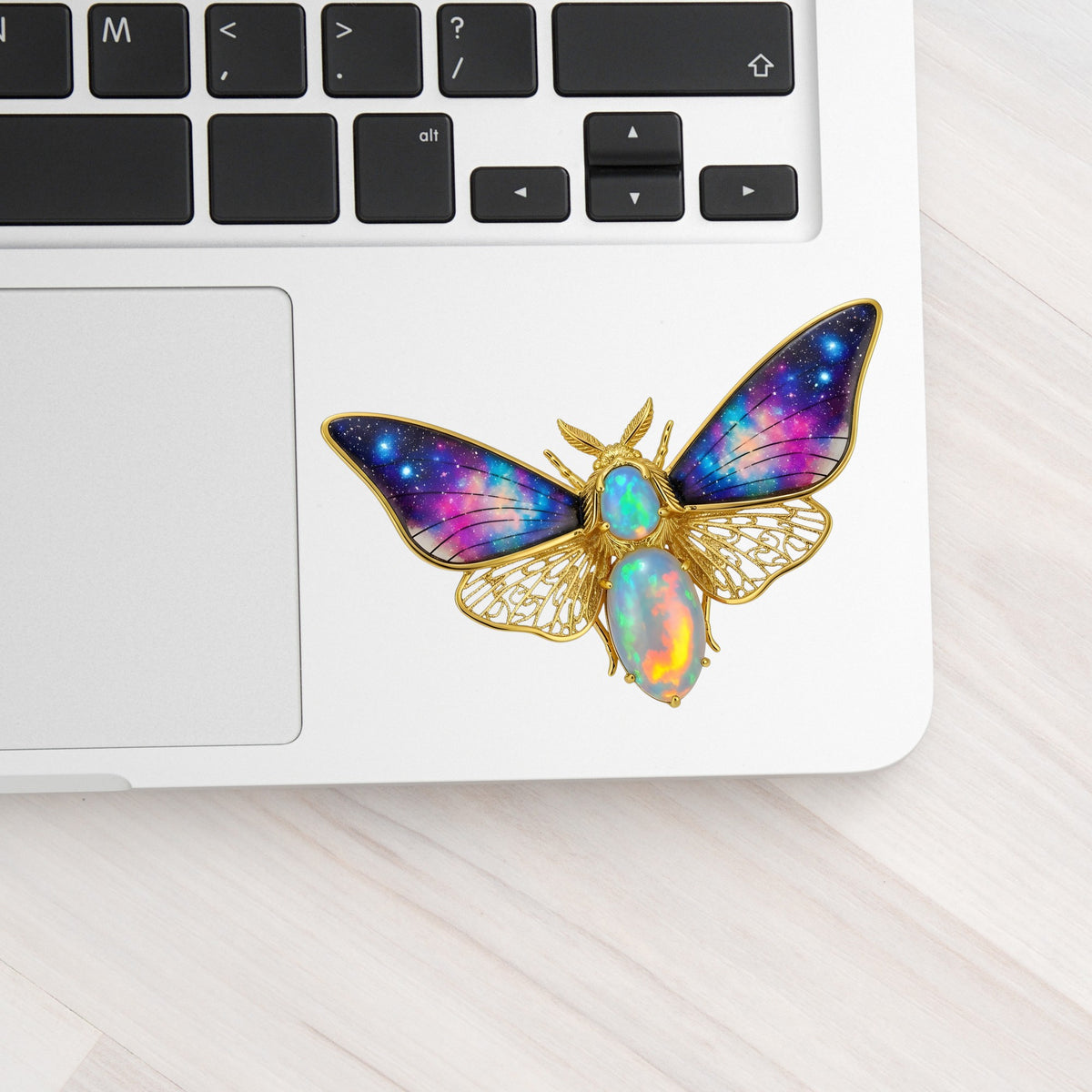 Opal Galaxy Moth UV DTF sticker applied to a silver laptop beside the keyboard