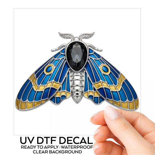 Silver Blue Enamel Moth UV DTF sticker on its backing card, held in hand