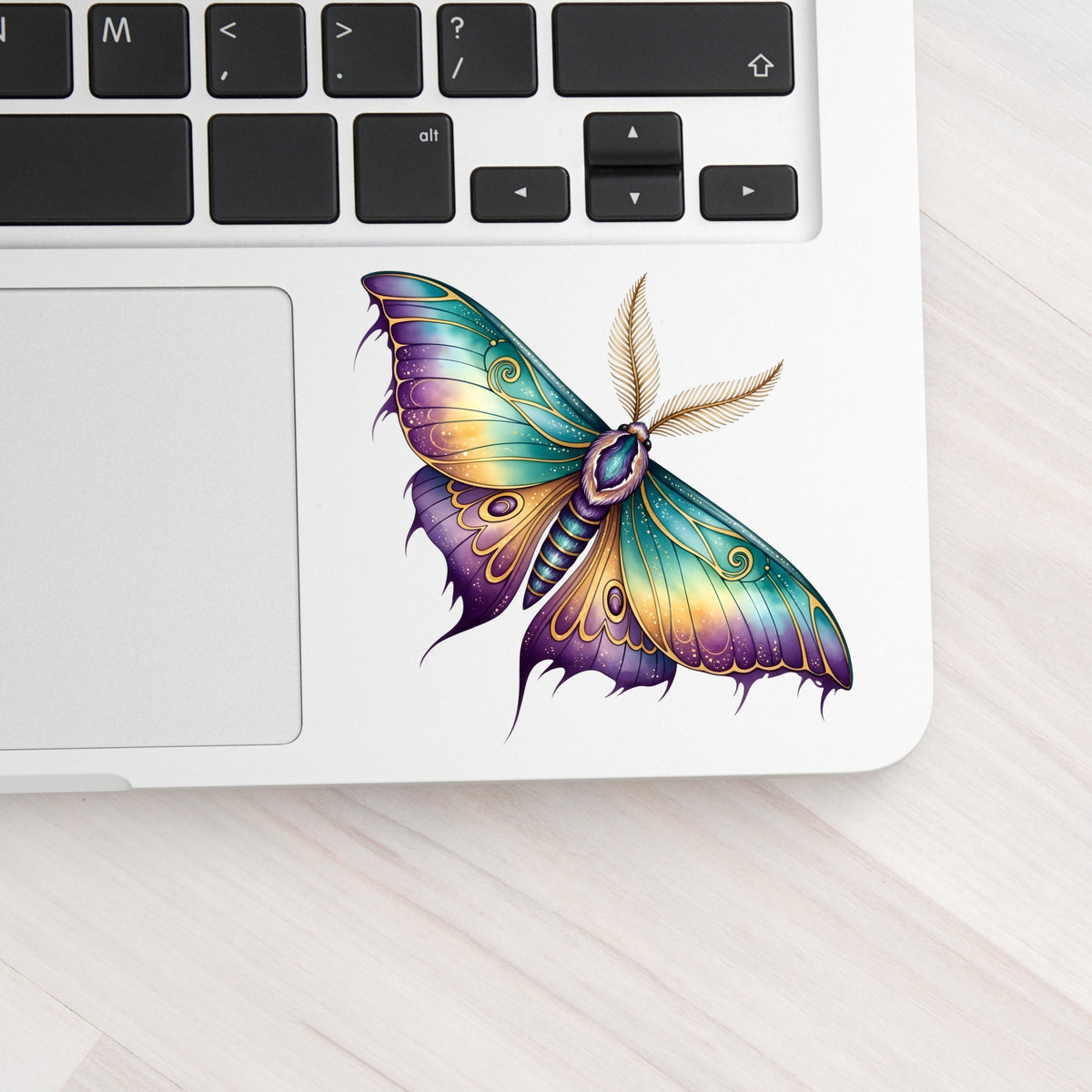 Watercolor Purple Teal Moth UV DTF sticker applied to a silver laptop beside the keyboard