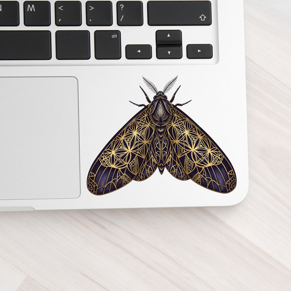 Sacred Geometry Moth UV DTF sticker applied to a silver laptop beside the keyboard
