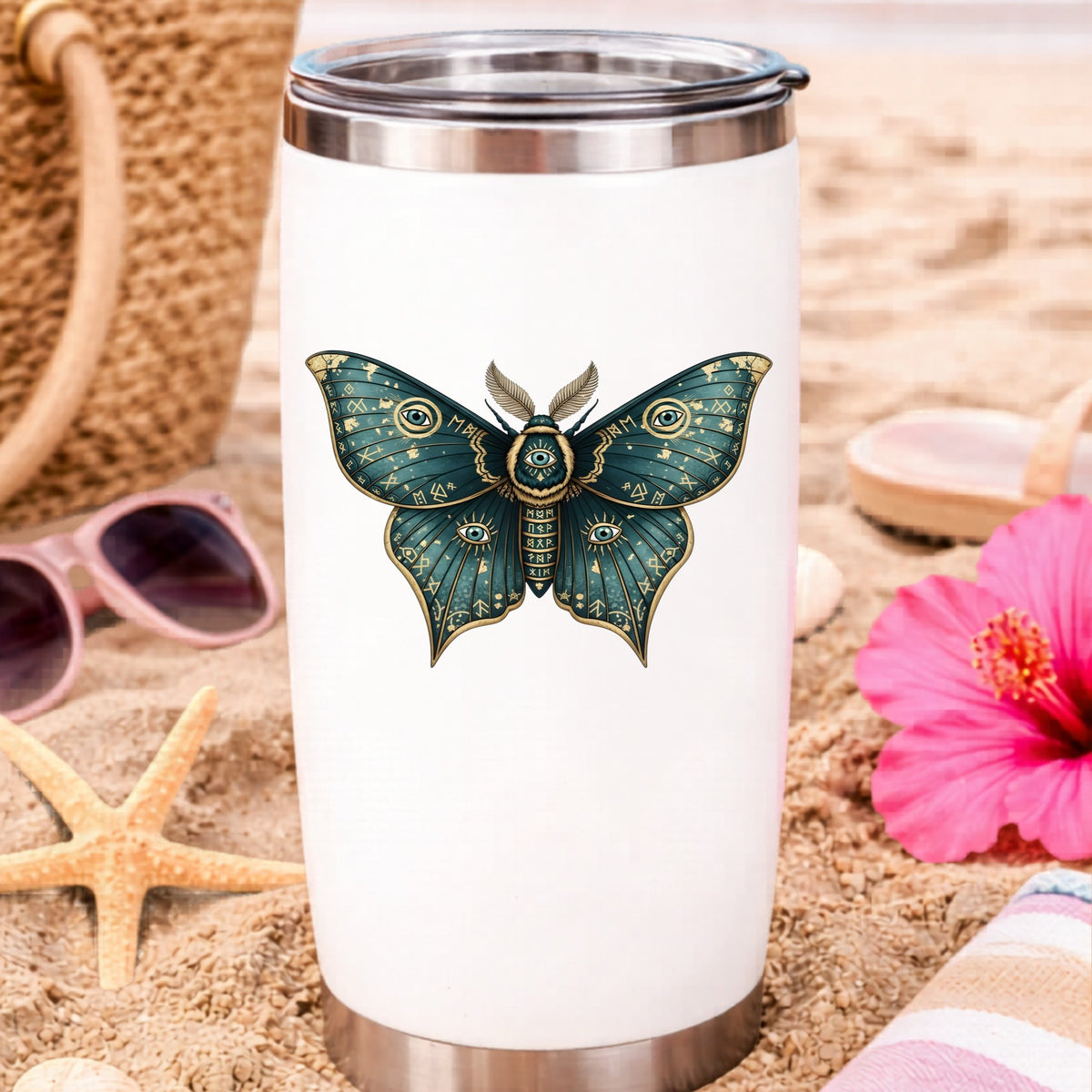 Teal Rune Moth All Seeing Eye UV DTF sticker applied to a white travel tumbler on beach sand