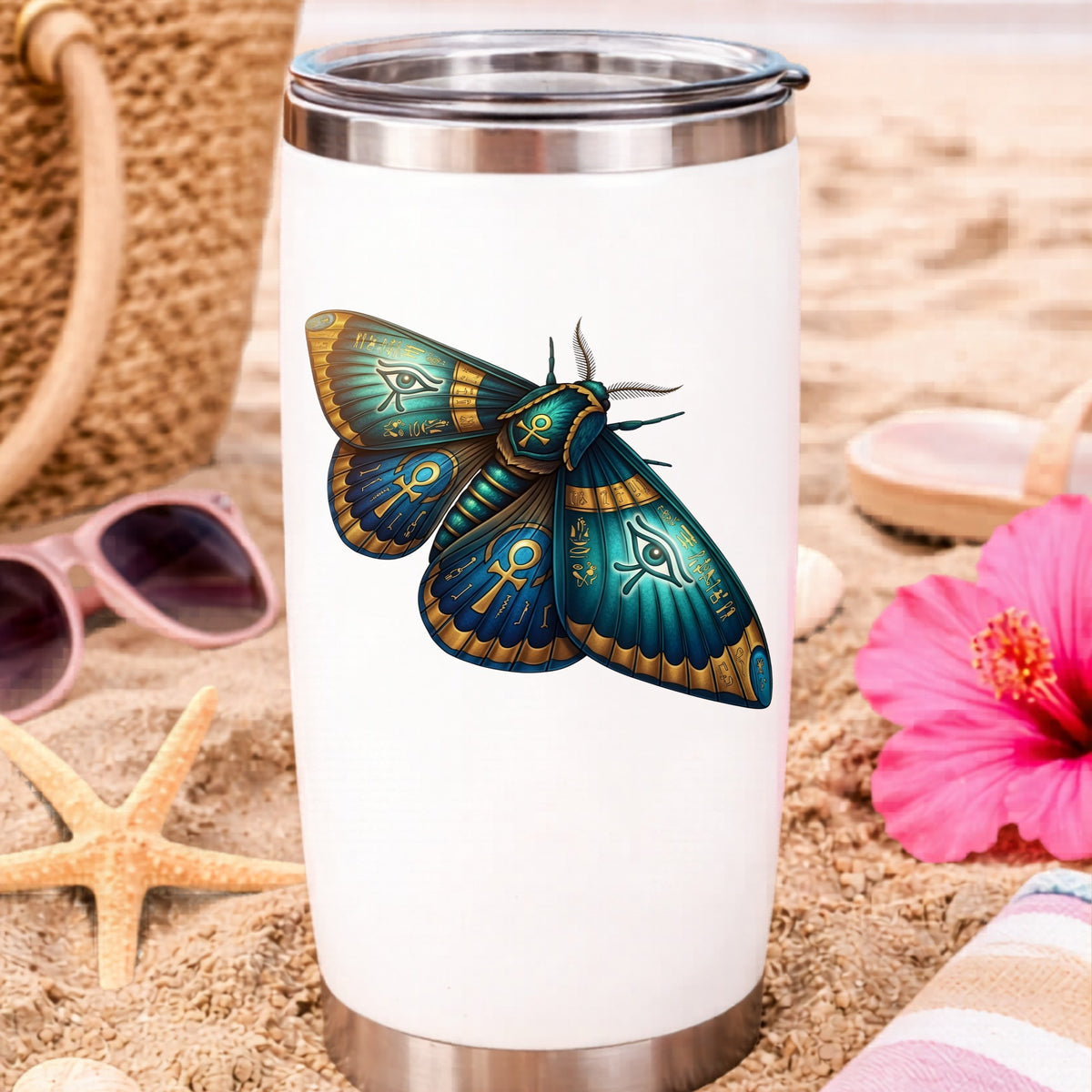Egyptian Eye Of Horus Moth UV DTF sticker applied to a white travel tumbler on beach sand