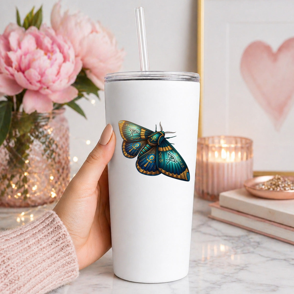 Egyptian Eye Of Horus Moth UV DTF sticker applied to a white straw tumbler beside pink peonies