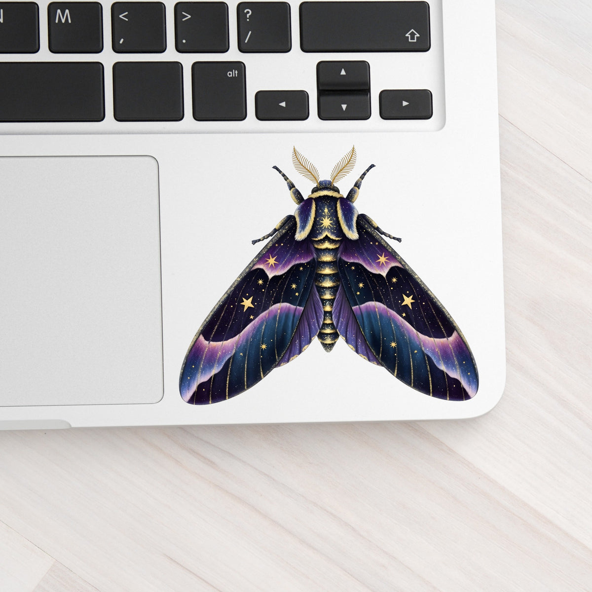 Night Sky Purple Moth UV DTF sticker applied to a silver laptop beside the keyboard