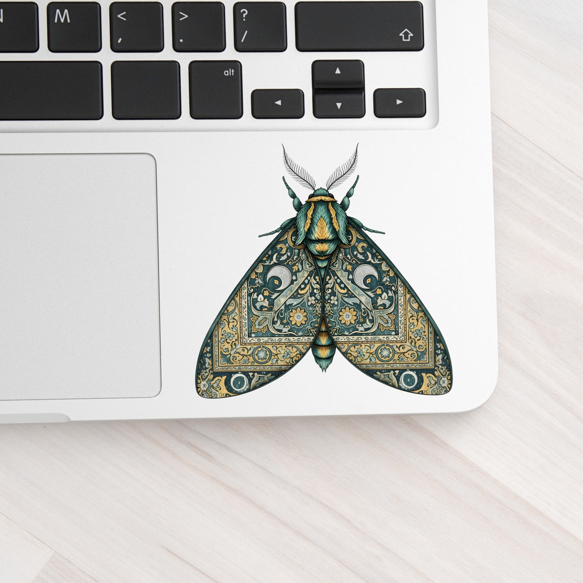 Green Damask Moth UV DTF sticker applied to a silver laptop beside the keyboard