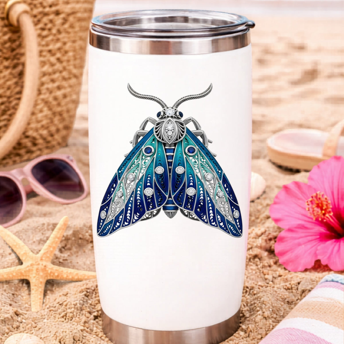 Silver Filigree Blue Moth UV DTF sticker applied to a white travel tumbler on beach sand