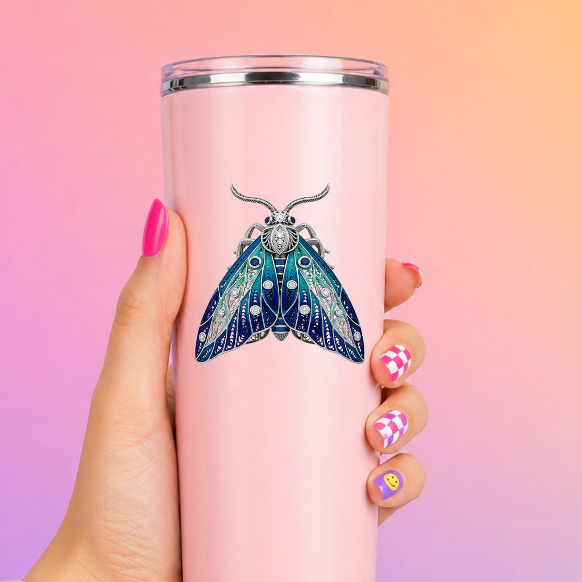 Silver Filigree Blue Moth UV DTF sticker applied to a tall pink tumbler on a pink and orange background