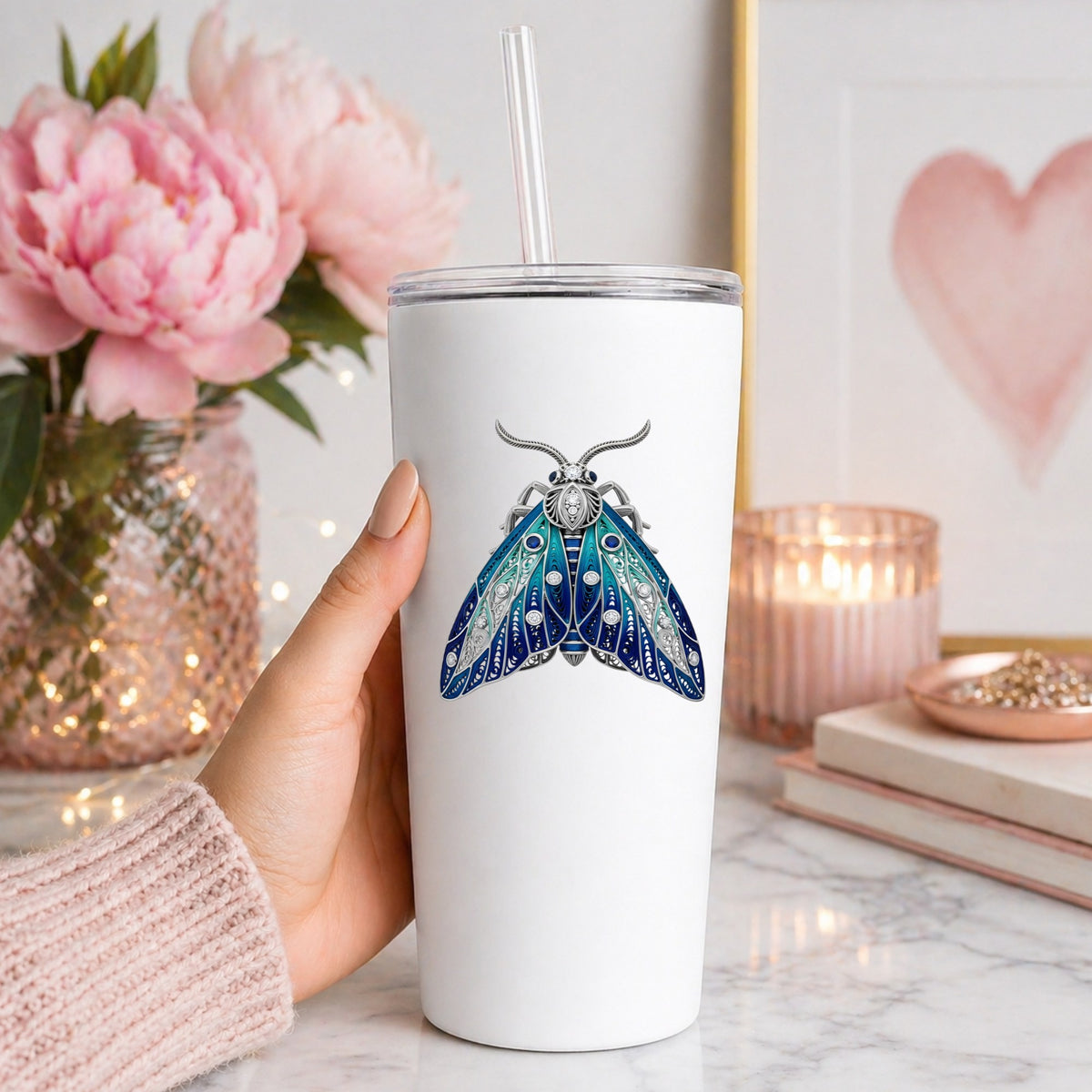 Silver Filigree Blue Moth UV DTF sticker applied to a white straw tumbler beside pink peonies